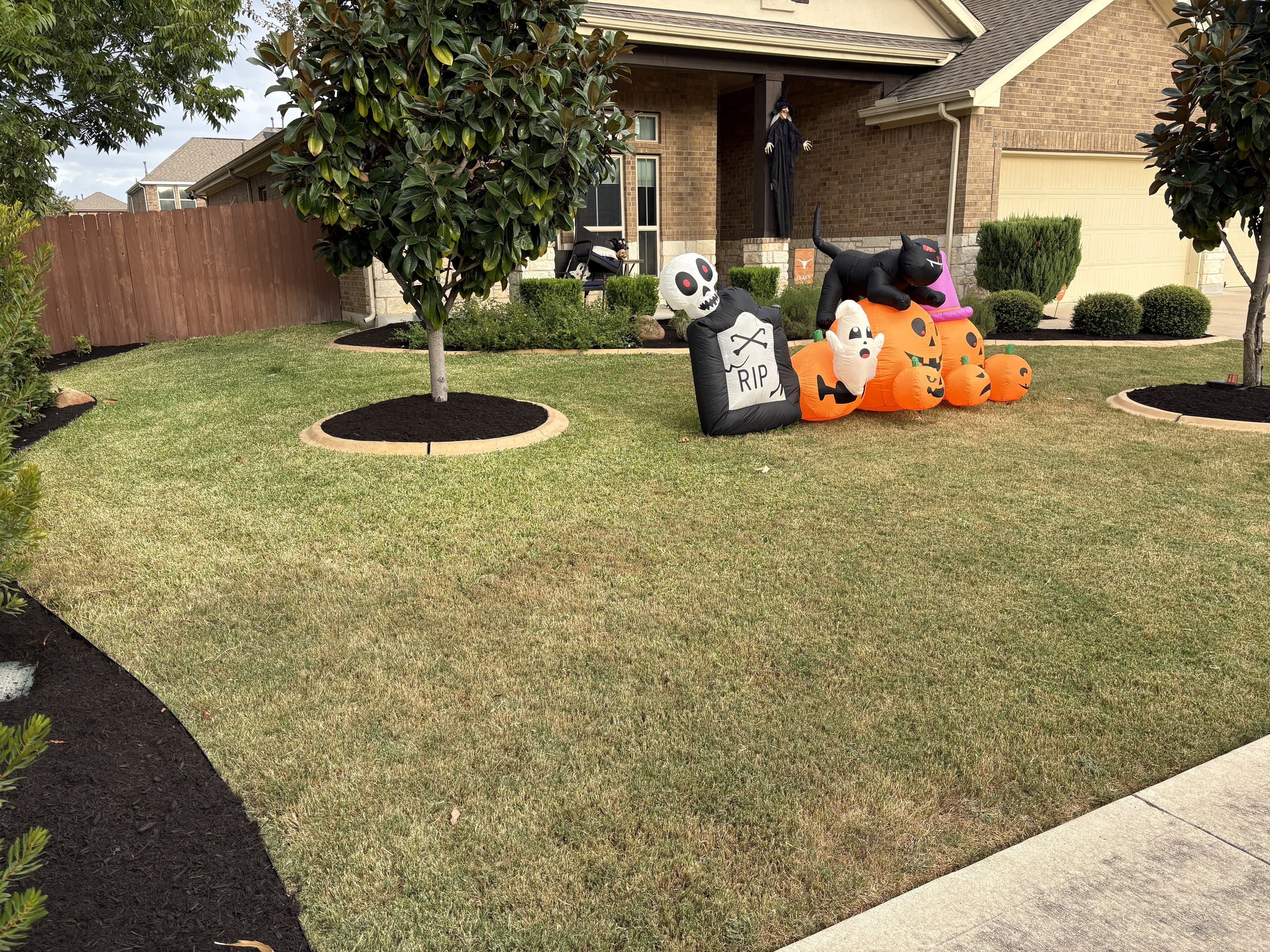 Inflatable Halloween decorations featuring a black cat, pumpkins, and a tombstone on a green lawn.